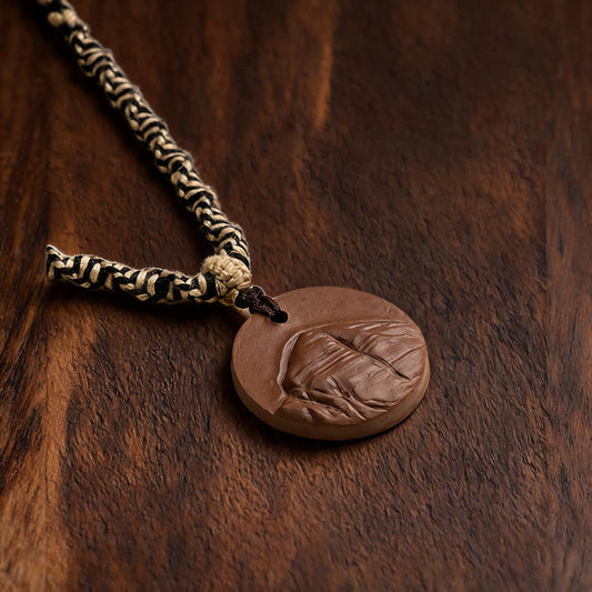 Mount Kailash brown clay tsatsa pendant necklace flat lay on dark wood