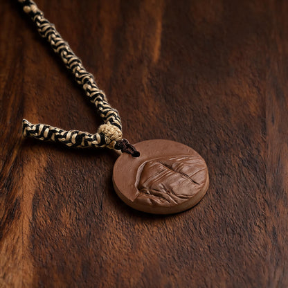 Mount Kailash brown clay tsatsa pendant necklace flat lay on dark wood
