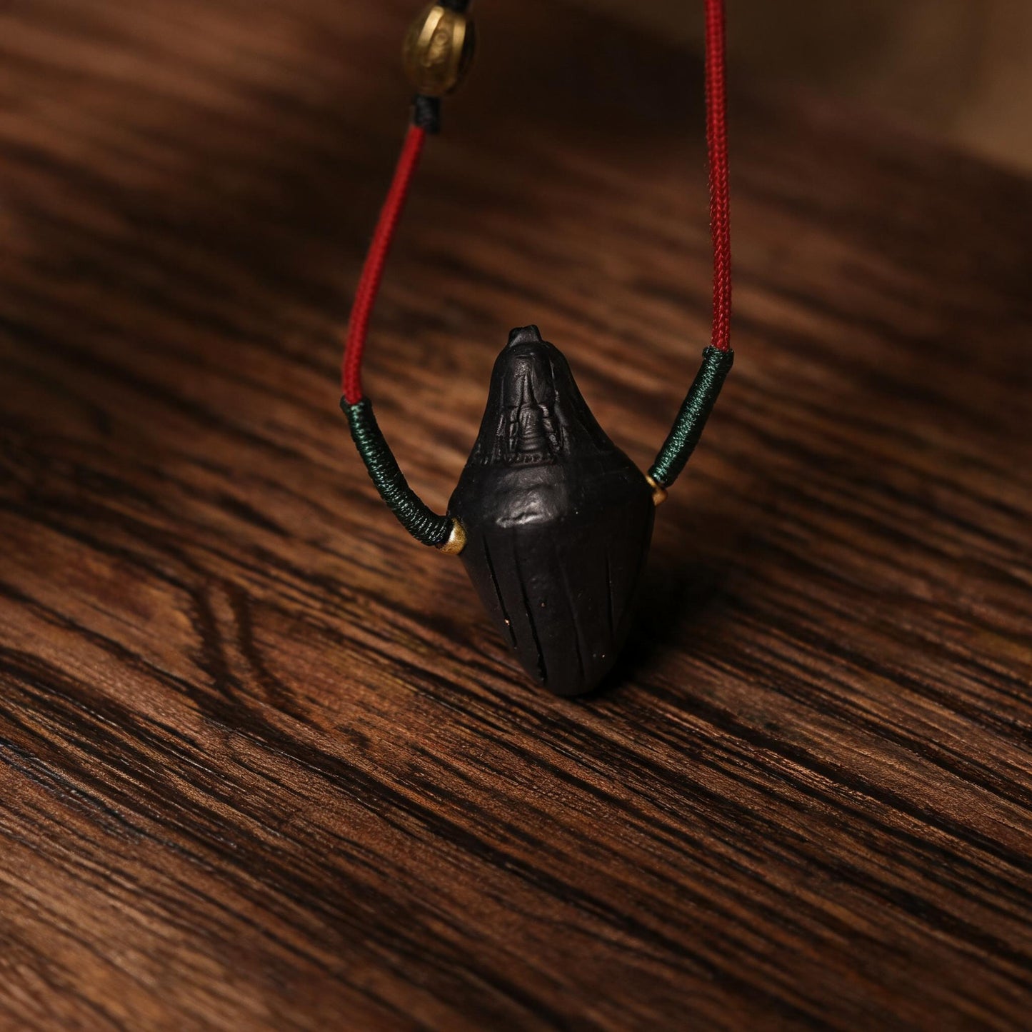 Angled side view of black pointed Nyangla clay tsatsa pendant