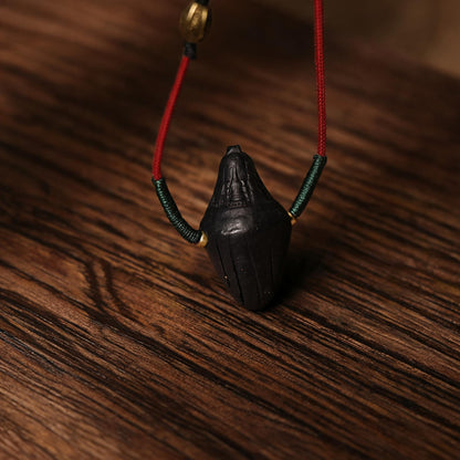 Angled side view of black pointed Nyangla clay tsatsa pendant